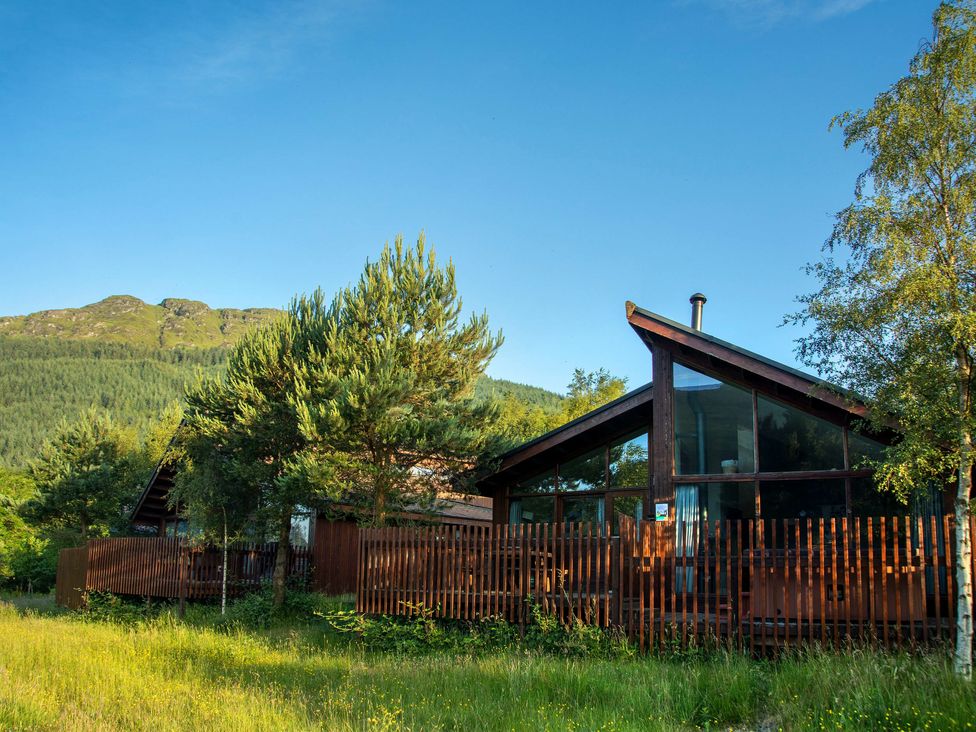 Two wooden houses with glass walls and fences surrounded by trees and grass with hills in the background at Ardgartan Argyll Golden Oak Ardgartan Loch Long