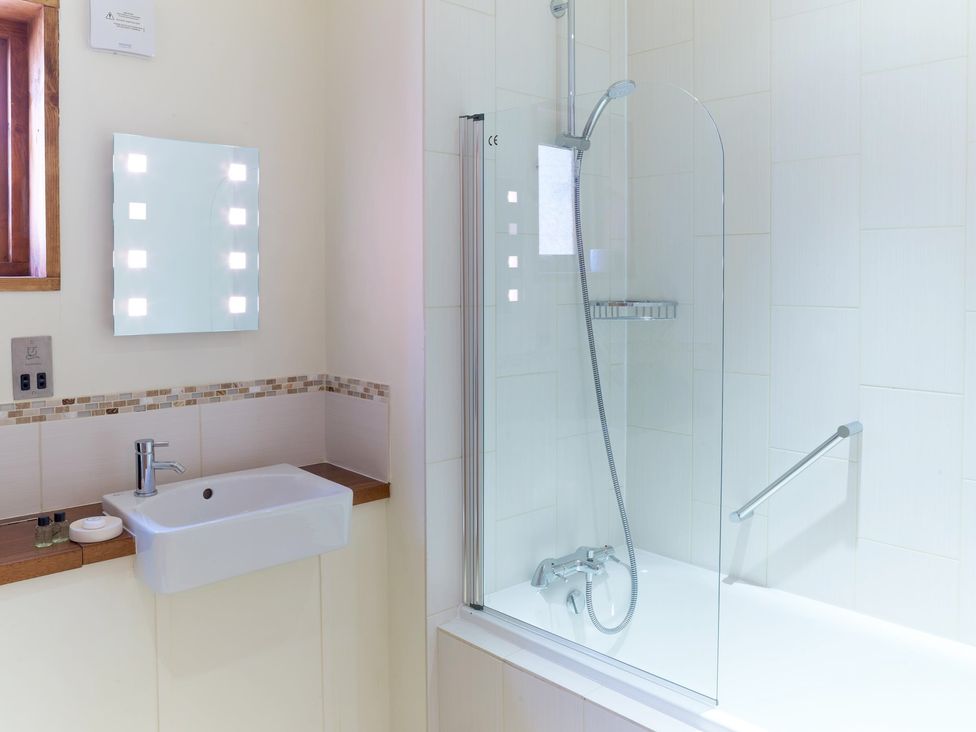 A bathroom with a sink and mirror with lights next to a bathtub and shower at Ardgartan Argyll Golden Oak Lochside Ardgartan Loch Long
