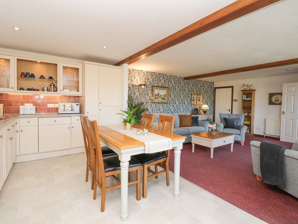 A kitchen with dining table and chairs adjoining a living room with sofas and coffee table at Woodland View in Muddiford near West Down