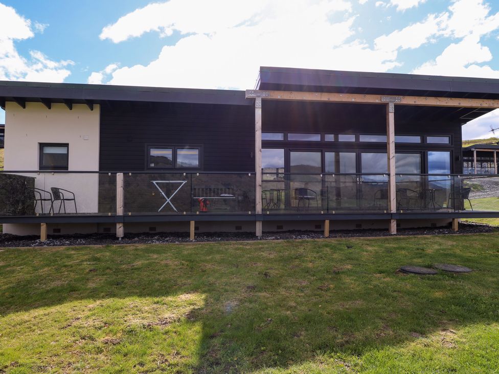 A modern single-story building with a glass balcony railing and outdoor chairs at 2 Strathtay Lodges in Aberfeldy