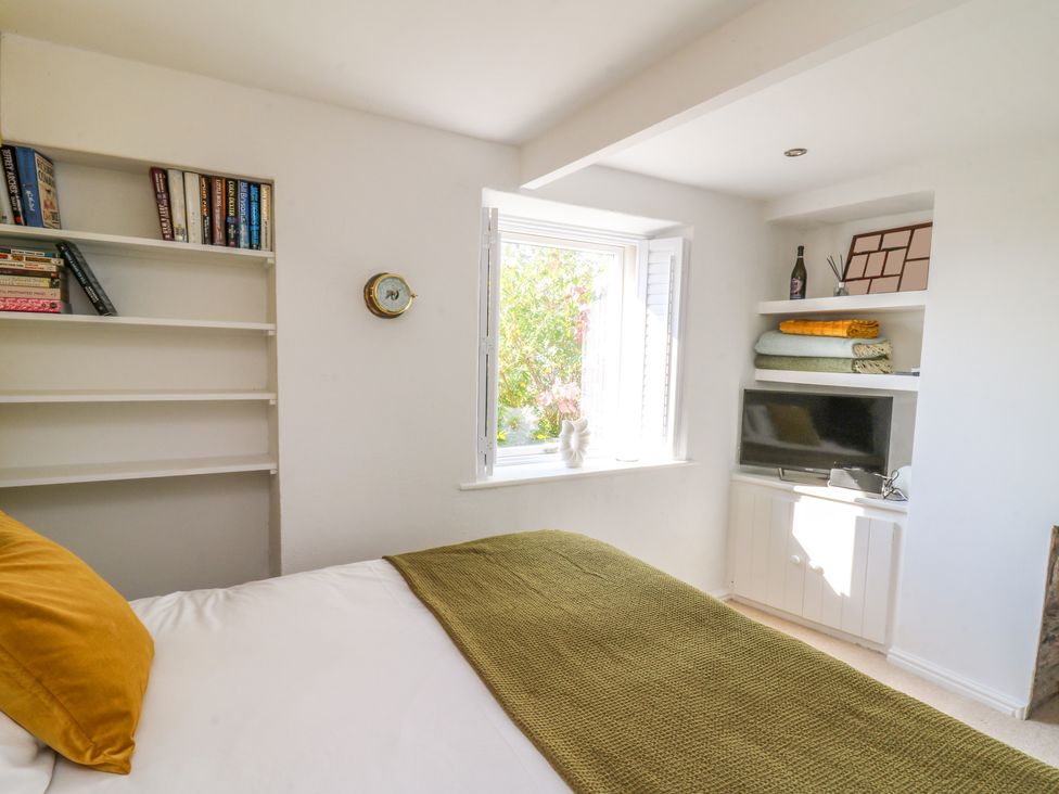 A bedroom with a bed covered by a green blanket and yellow pillow and shelves holding books and a television at 1 Gibraltar Terrace in Aberdovey