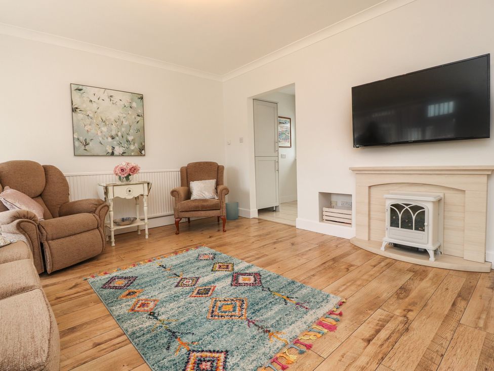 A living room with brown armchairs a side table with flowers a fireplace a wall mounted tv and a patterned rug on wooden floor at 14 Berwick Road in Lytham St Annes