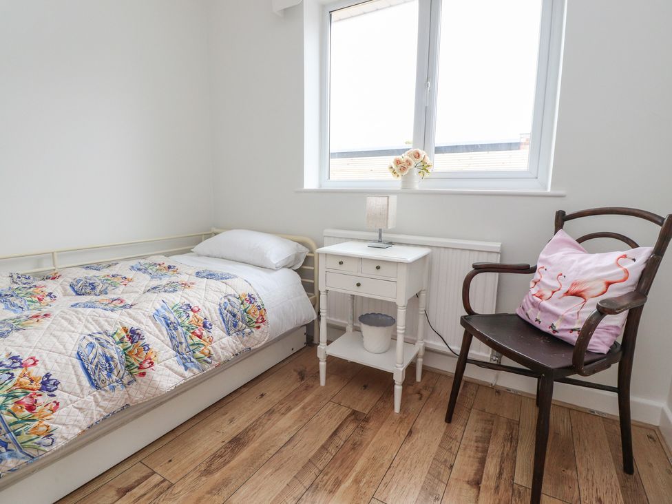A small bedroom with a single bed a white bedside table with a lamp a wooden chair with a pink flamingo pillow and a window with flowers on the sill at 14 Berwick Road in Lytham St Annes