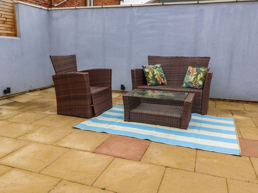 An outdoor patio area with brown wicker furniture including a loveseat with two patterned cushions an armchair and a glass-top coffee table on a blue and white striped rug at 14 Berwick Road in Lytham St Annes