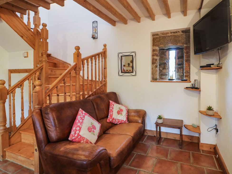 A living room with a brown leather sofa two red floral cushions wooden stairs and a wall-mounted television at The Abraham in Castledermot County Kildare