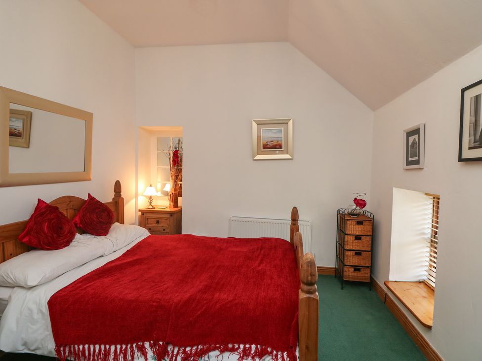 A bedroom with a wooden bed with red pillows and blanket bedside tables with lamps and basket storage at The Abraham in Castledermot County Kildare
