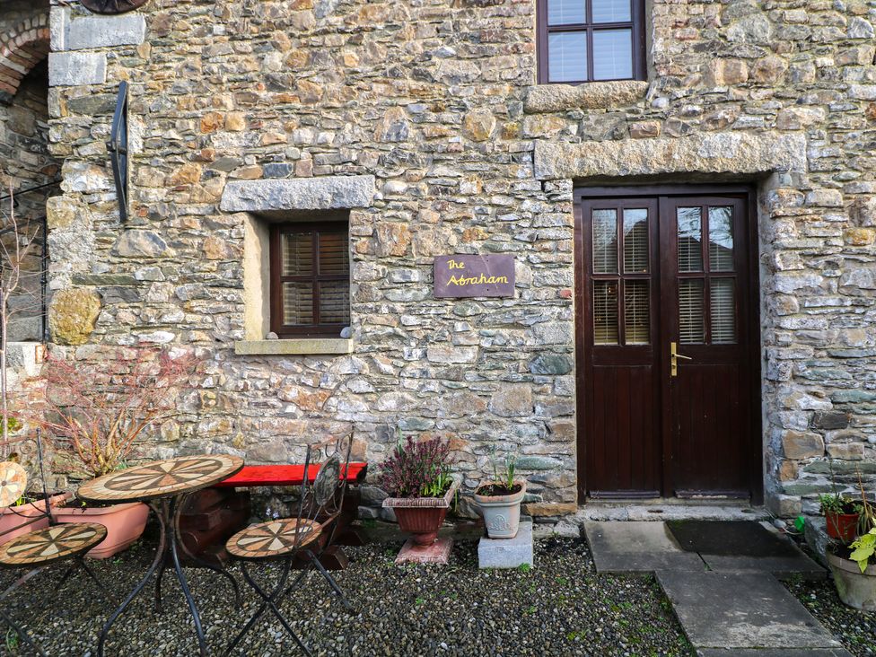 A stone exterior wall with a wooden double door and window with small metal table and chairs and plants at The Abraham in Castledermot County Kildare