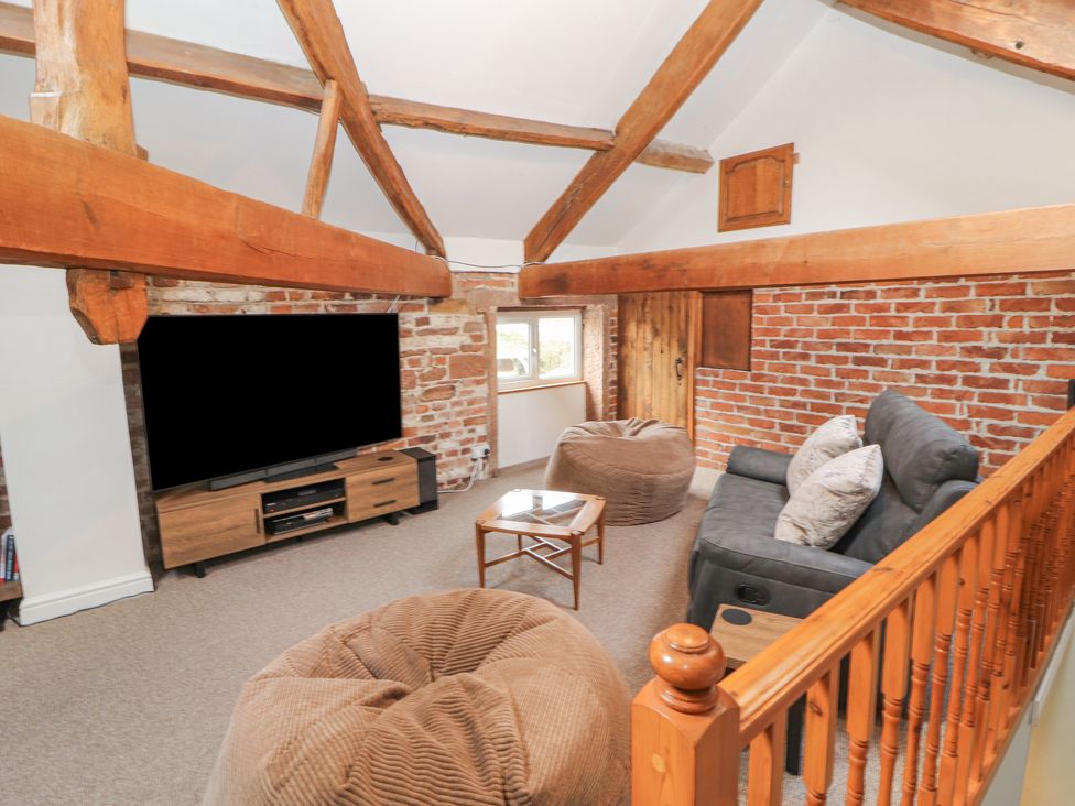 A loft living area with wood beams a large TV bean bag chairs a small wooden table a gray sofa and exposed brick walls at The Hideaway @ Waverton Villa in Wigton