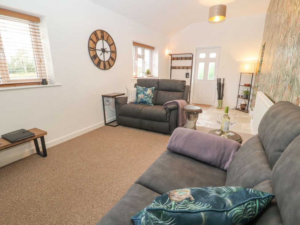 A sitting room with two grey sofas and a wooden clock on the wall at The Hideaway @ Waverton Villa in Wigton