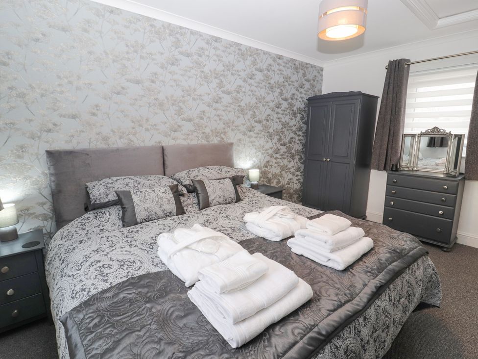 A bedroom with a double bed with folded towels on it and a wardrobe and dresser with mirror at The Hideaway @ Waverton Villa in Wigton