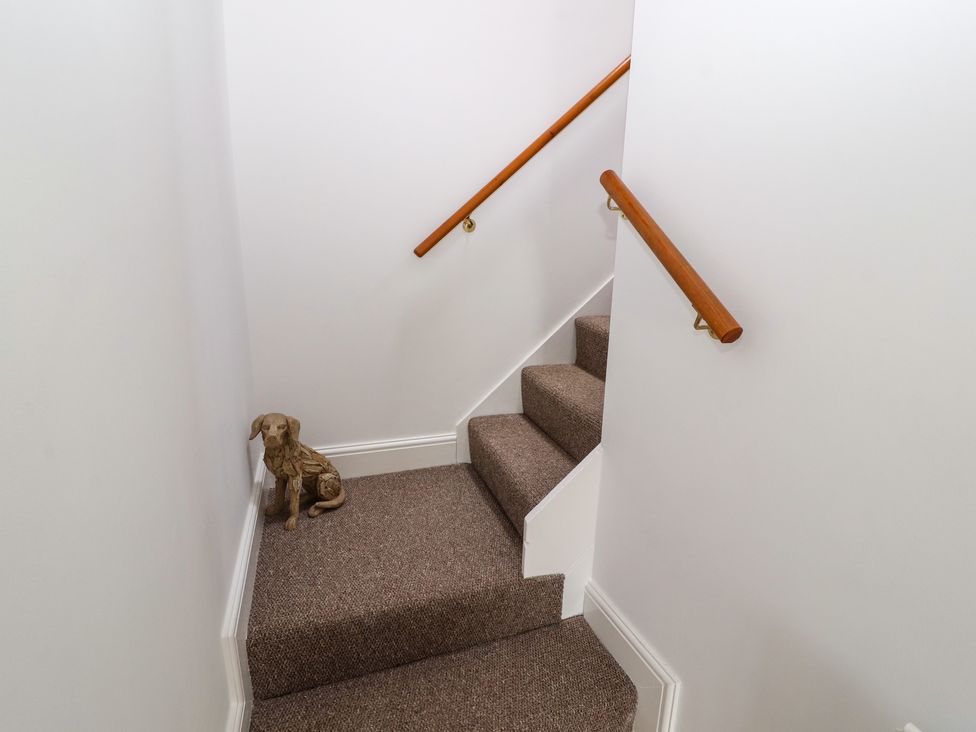 A carpeted staircase with wooden handrails and a dog statue at The Hideaway @ Waverton Villa in Wigton