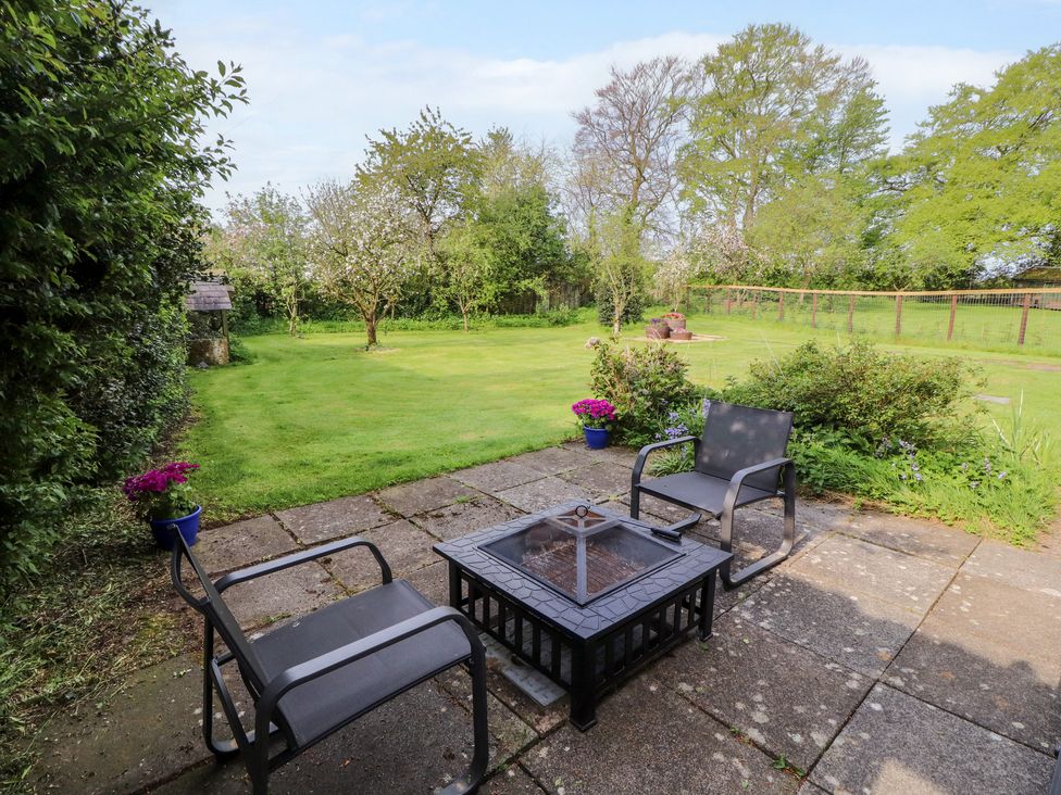 A patio with two chairs and a fire pit overlooking a grassy garden with trees and potted flowers at The Hideaway @ Waverton Villa in Wigton