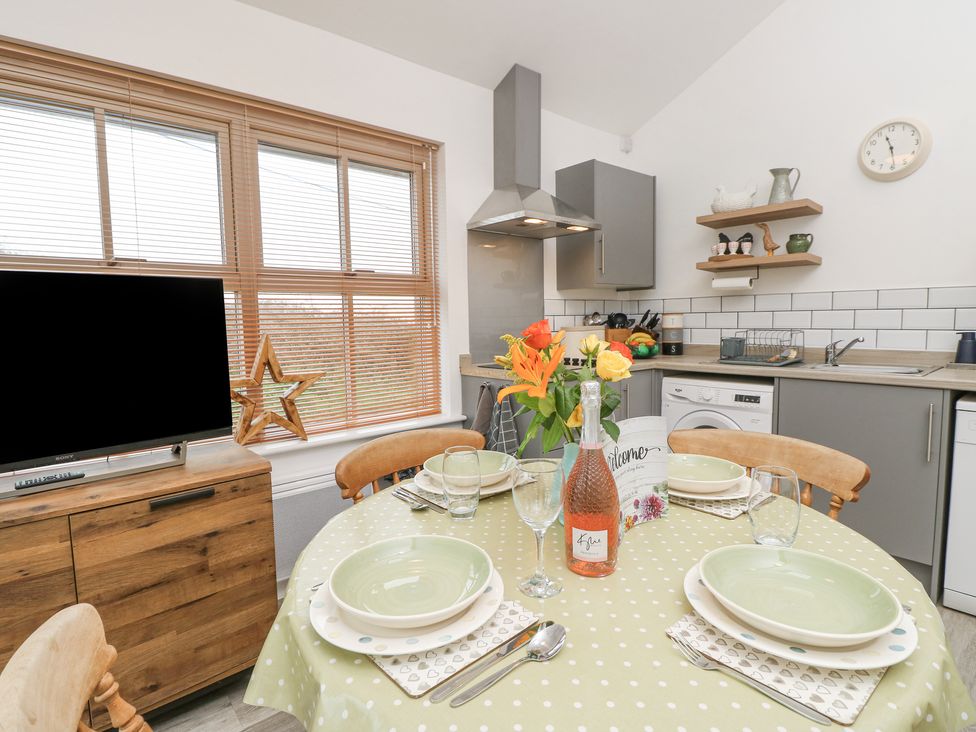 A kitchen and dining area with a round table set with plates and glasses at The Pepper Pot Retreat in Head Down near Niton