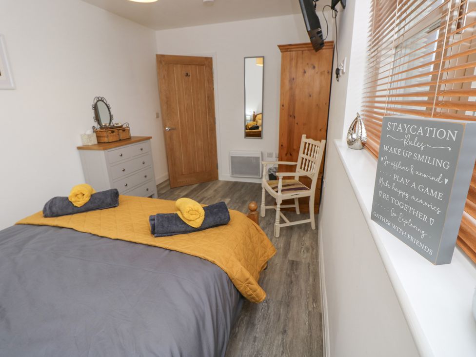 A bedroom with a bed with yellow and gray bedding a dresser a wooden door a chair a tall wooden wardrobe and a sign on the windowsill at The Pepper Pot Retreat Head Down near Niton