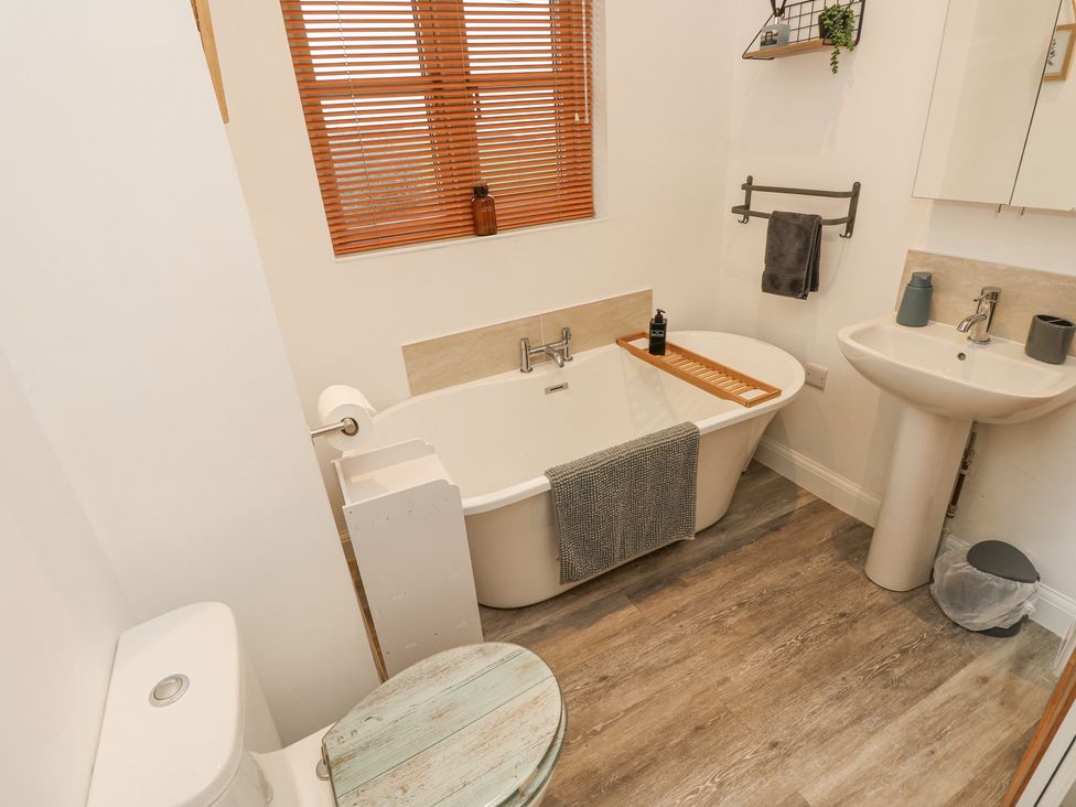 A bathroom with a bathtub a pedestal sink a toilet a small round wooden table and wooden blinds at The Pepper Pot Retreat in Head Down near Niton