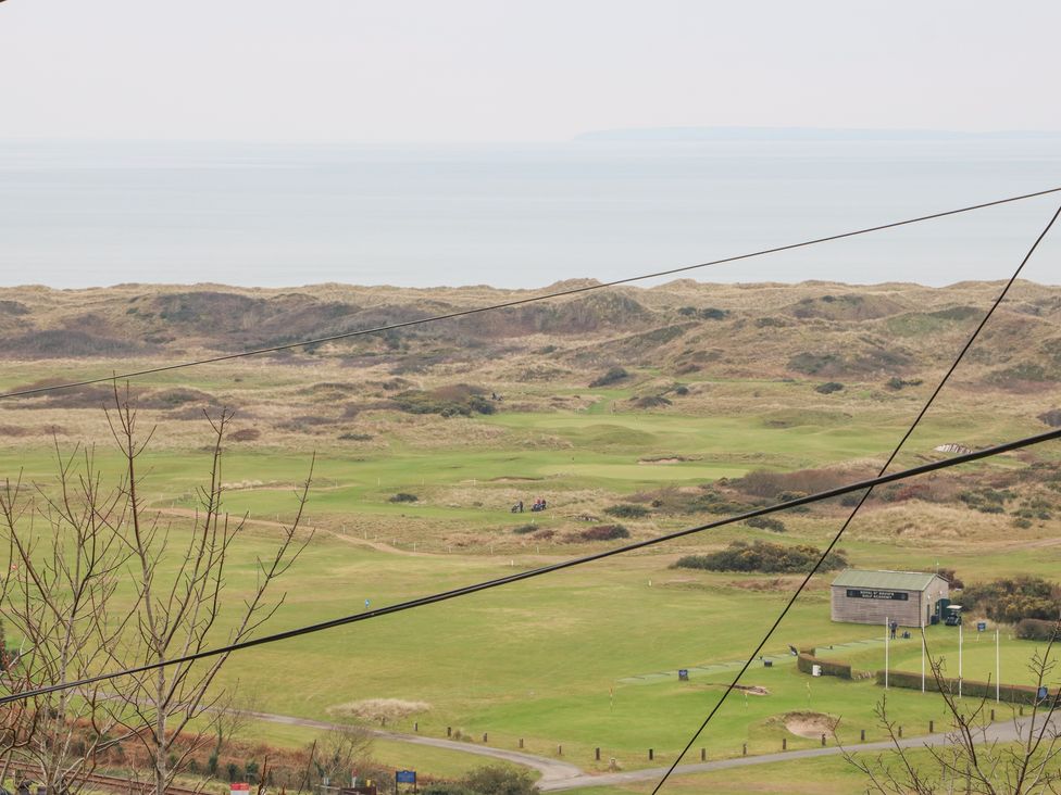 A golf course with a building and flagpoles near a coastal area with dunes and the sea in the background at Hafod Y Bryn in Harlech