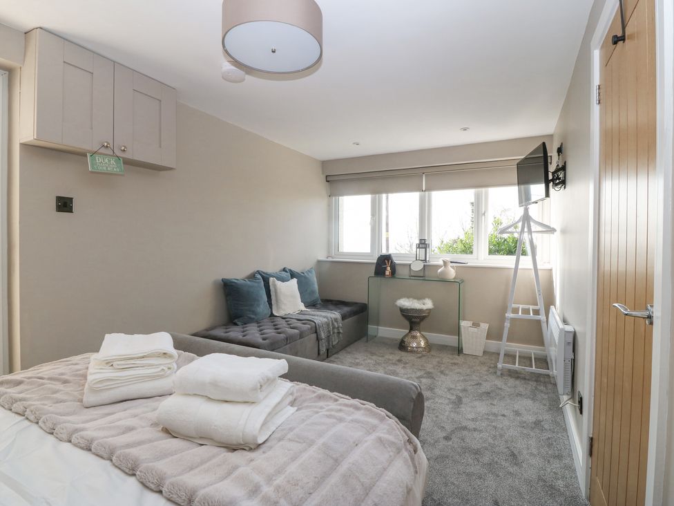 A bedroom with a bed and folded towels a bench with pillows a glass desk and a mounted television at Hafod Y Bryn in Harlech
