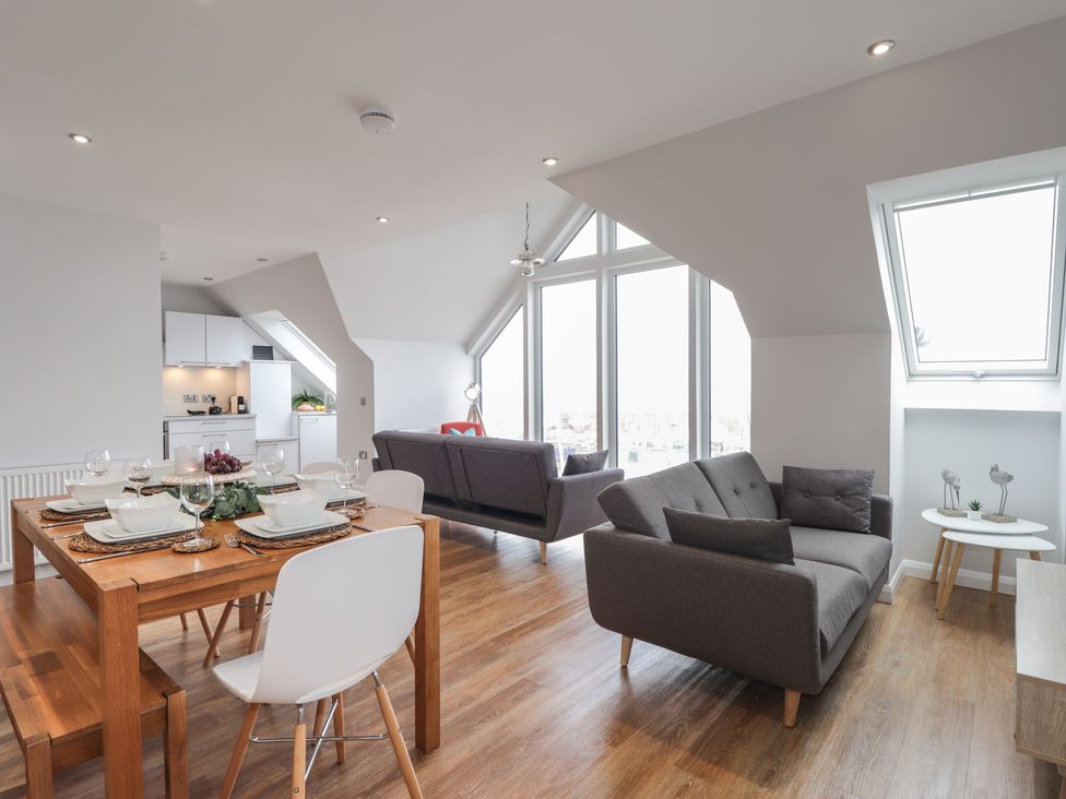 An open plan living and dining area with grey sofas wooden dining table and white chairs at Spinnaker in Lossiemouth