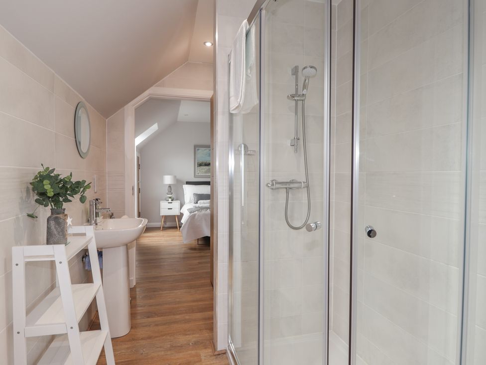 A bathroom with a shower, sink, mirror, and shelves with a view into a bedroom at Spinnaker in Lossiemouth