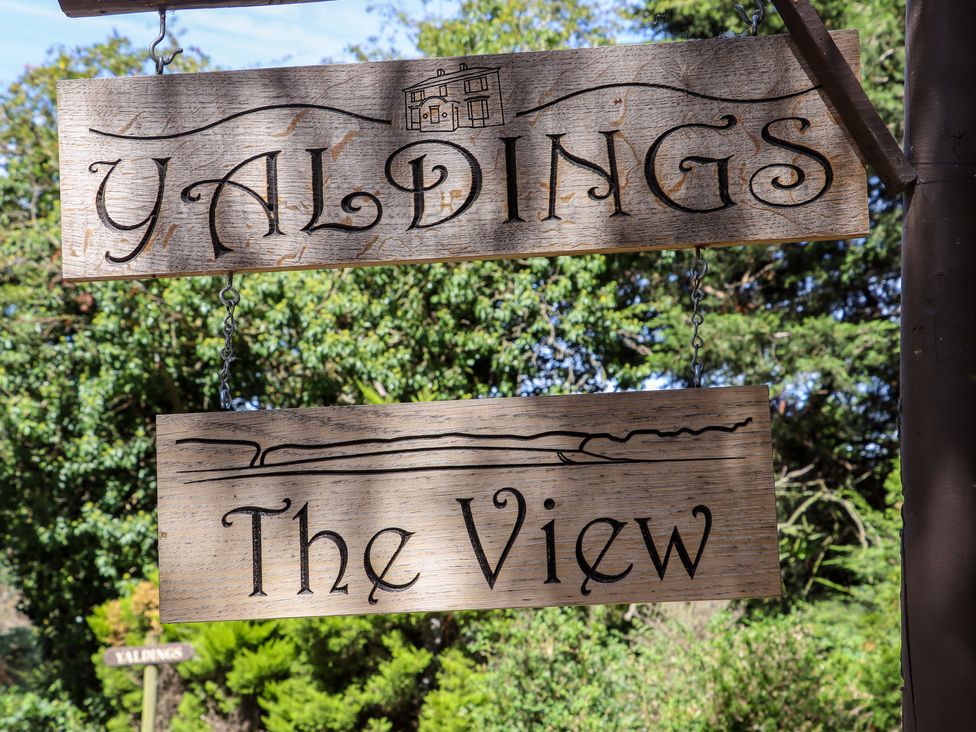 A wooden sign with the words Yaldings and The View hanging outdoors with greenery in the background