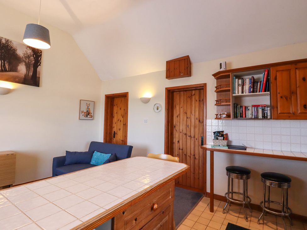 A kitchen area with wooden cabinets stools a blue sofa and a tiled countertop at The View in Goodnestone near Faversham