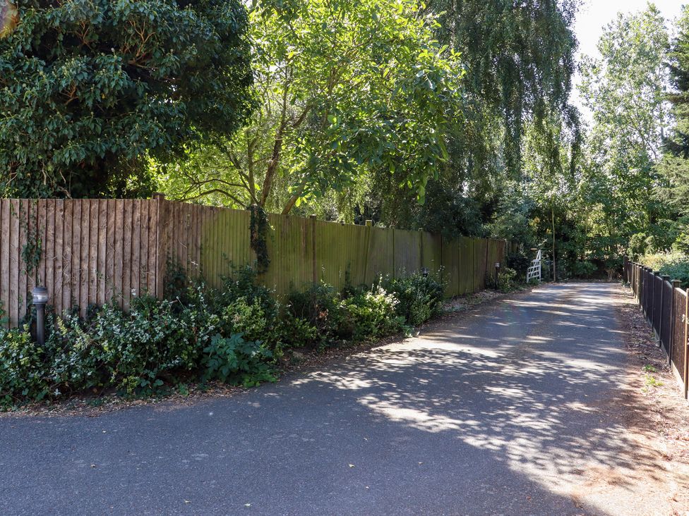 A paved road bordered by wooden fences and trees with vegetation along the sides at The View in Goodnestone near Faversham