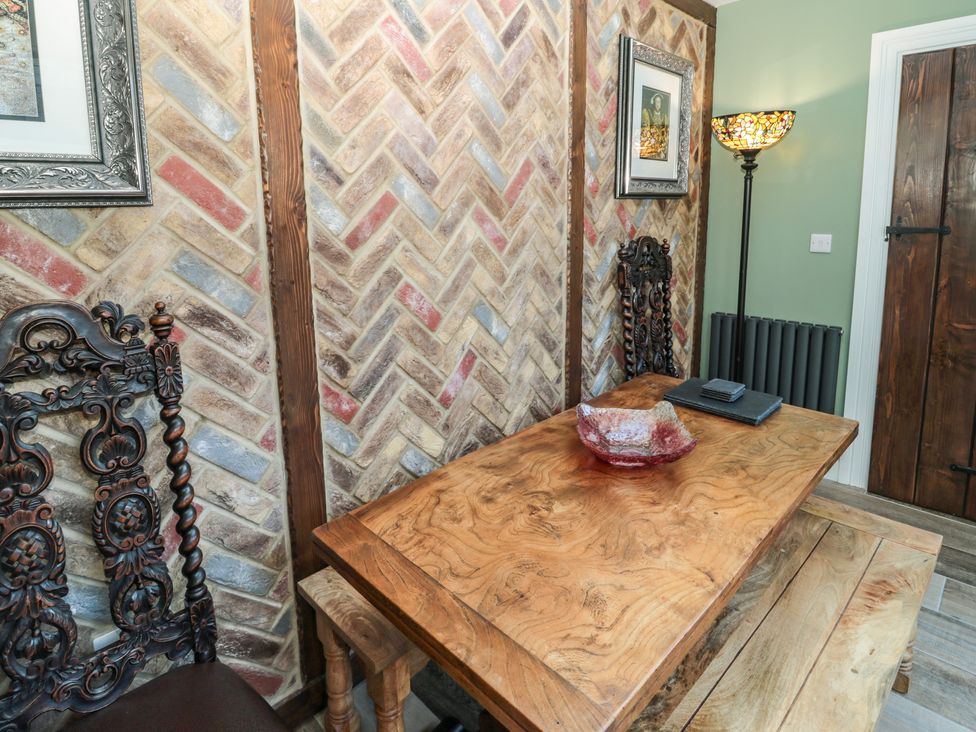A dining area with a wooden table, carved wooden chairs, a bench, a floor lamp, framed pictures on the wall at Sunflowers in Earsdon near Whitley Bay