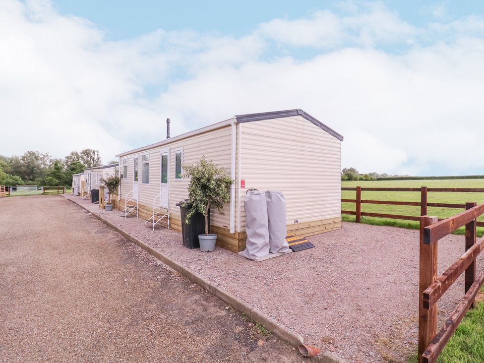 Two beige mobile homes with steps and potted plants outside next to a wooden fence in a rural area at The Richmond in St Osyth