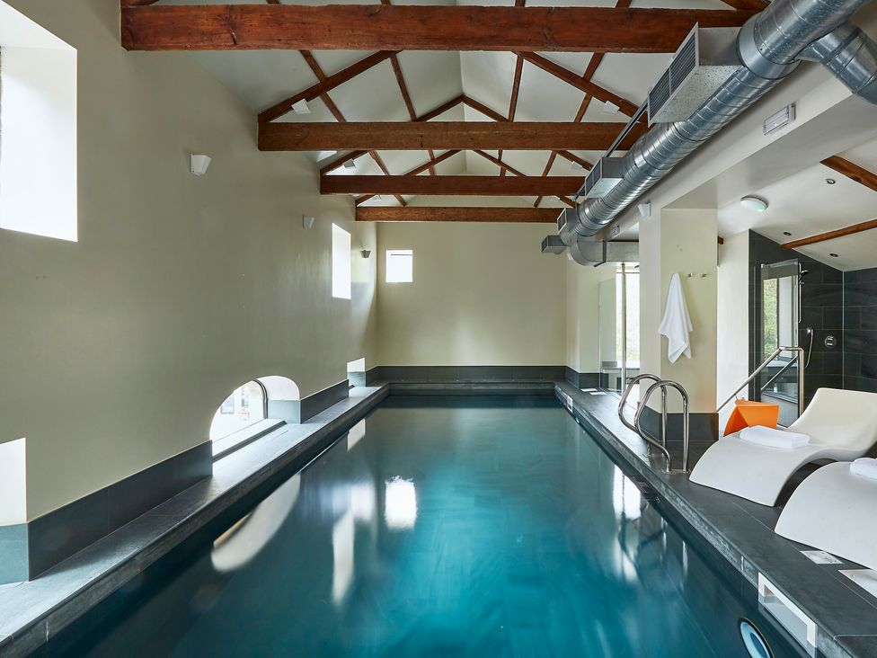 An indoor swimming pool with lounge chairs and exposed wooden beams at Oughtershaw Hall in Hawes