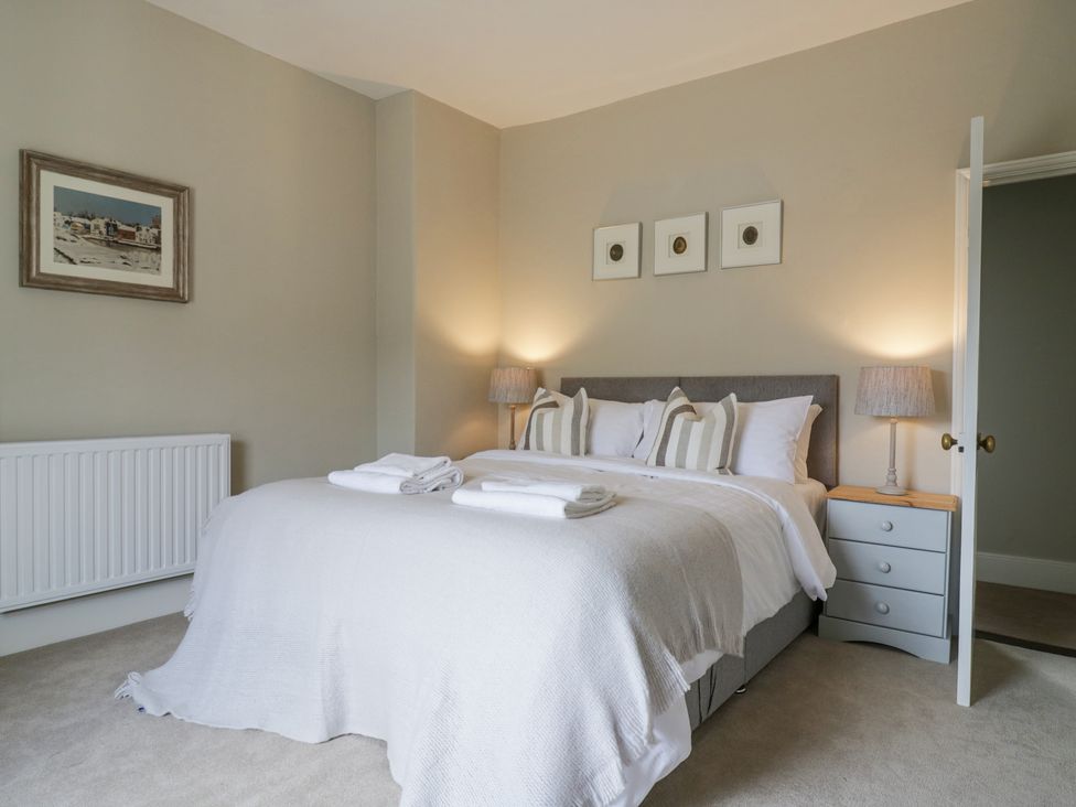 A bedroom with a double bed, bedside table with lamp, towels on bed, three framed pictures above bed, radiator on wall at Knights Farm in Harkstead