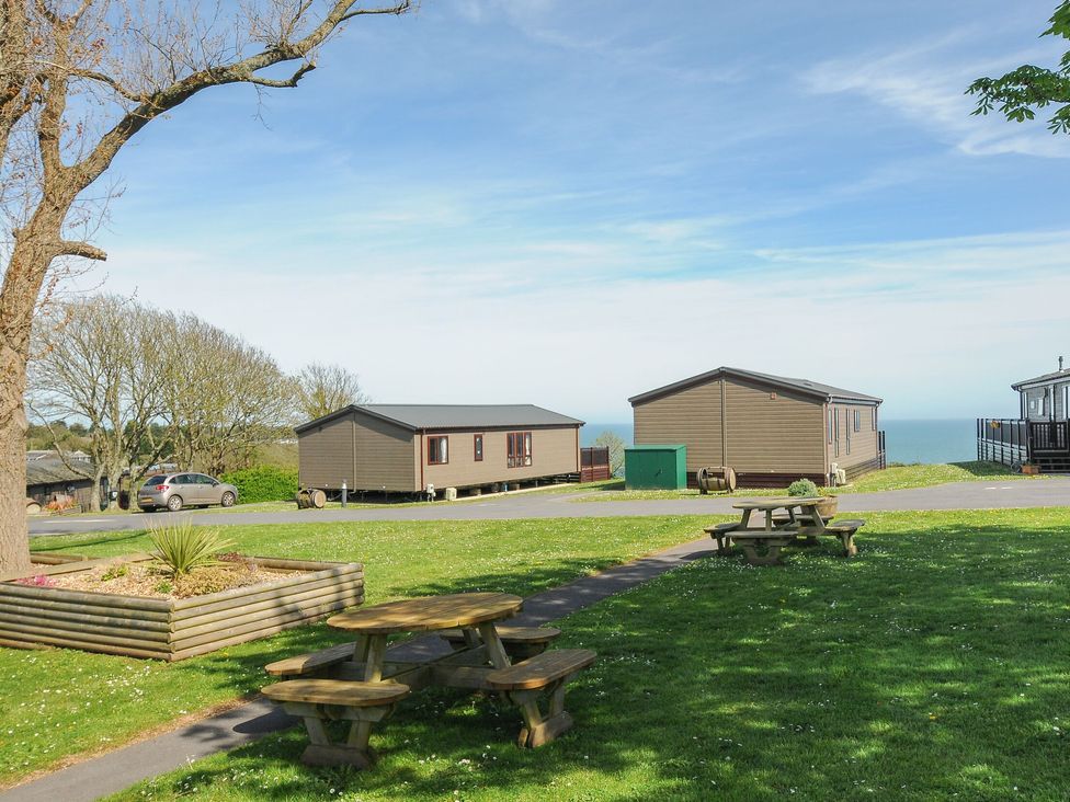 A picnic area with wooden tables and cabins on grassy land overlooking the sea at Lodge 68 at Riviera Bay Coastal Retreat in Brixham