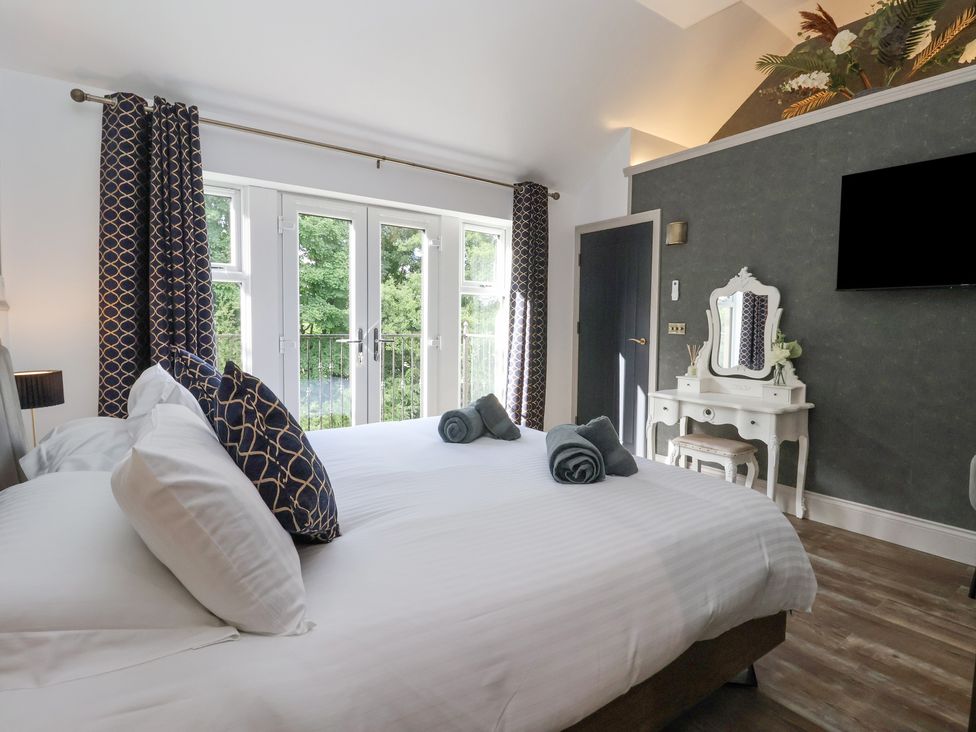 A bedroom with a large bed and rolled towels near glass doors and a white dressing table at Waters Edge Lock View in Gargrave