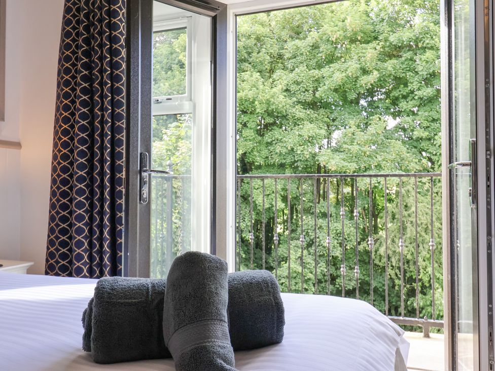 A bedroom with towel rolls on the bed and open balcony doors showing trees outside at Waters Edge Lock View in Gargrave