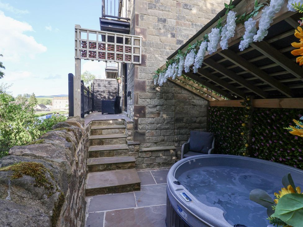 An outdoor patio area with stone steps leading to a seating area and a covered hot tub with floral decorations at Waters Edge Lock View in Gargrave