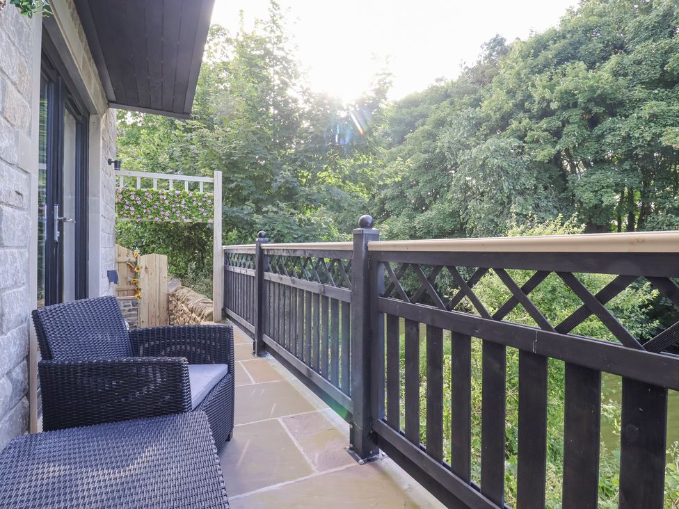 A balcony with two black wicker chairs and a black railing overlooking trees at Waters Edge Lock View in Gargrave