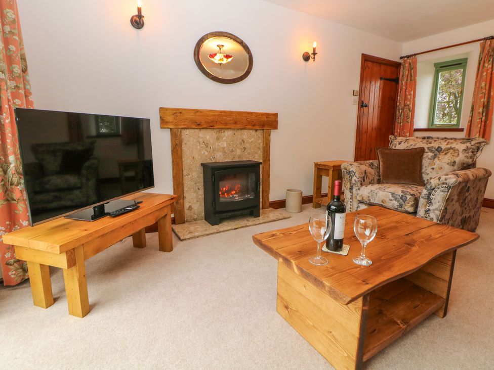 A sitting room with a patterned armchair wooden tables a TV a fireplace and a bottle of wine with glasses on the table at Temperance Croft in Wadshelf near Chesterfield