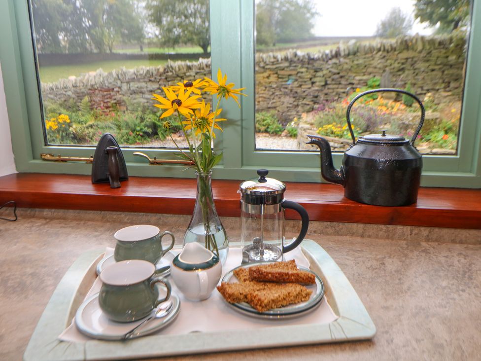 A kitchen counter with a tray holding two cups and saucers spoons a glass pot a sugar bowl a plate of cereal bars and a vase with yellow flowers at Temperance Croft in Wadshelf near Chesterfield