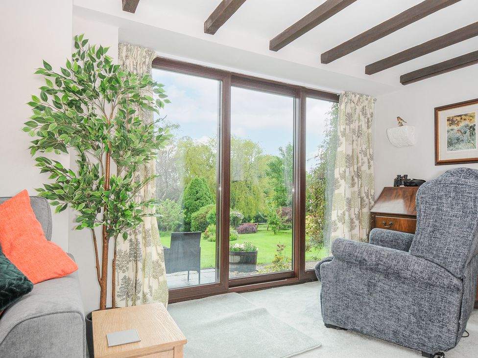 A living room with a gray armchair a green plant and large windows looking out to a garden at Manor Barn in Saltash