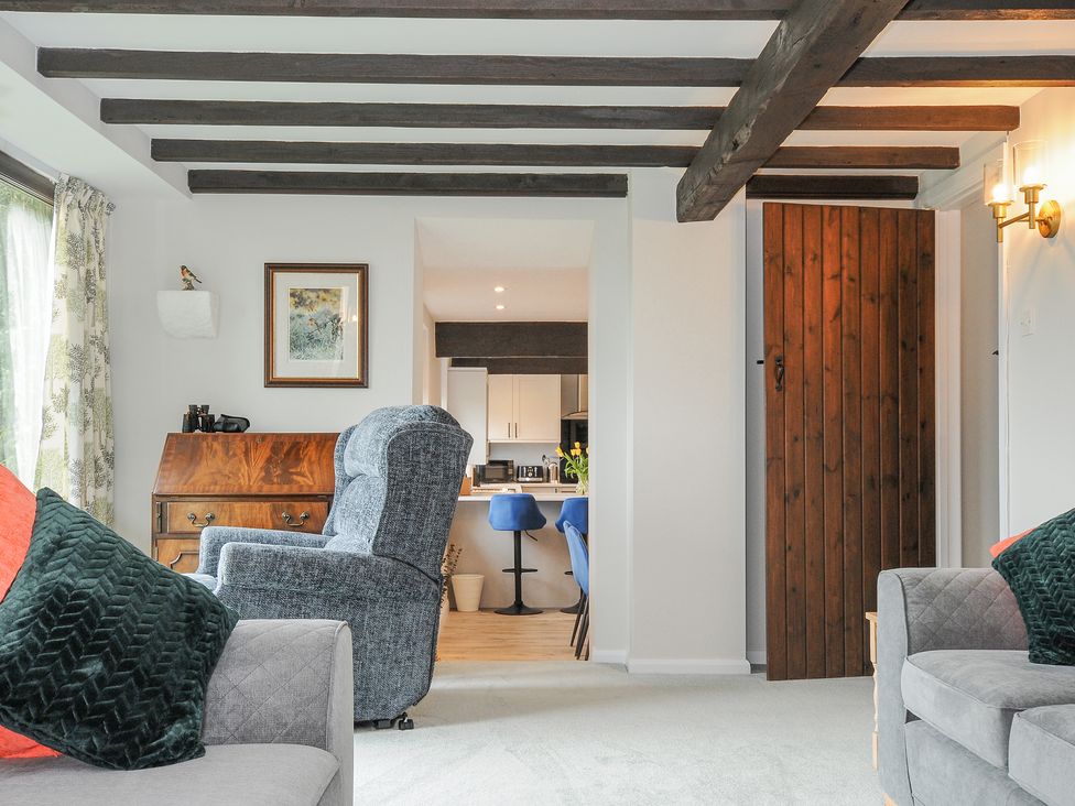 A living room with gray and blue armchairs wooden door and kitchen area visible at Manor Barn in Saltash