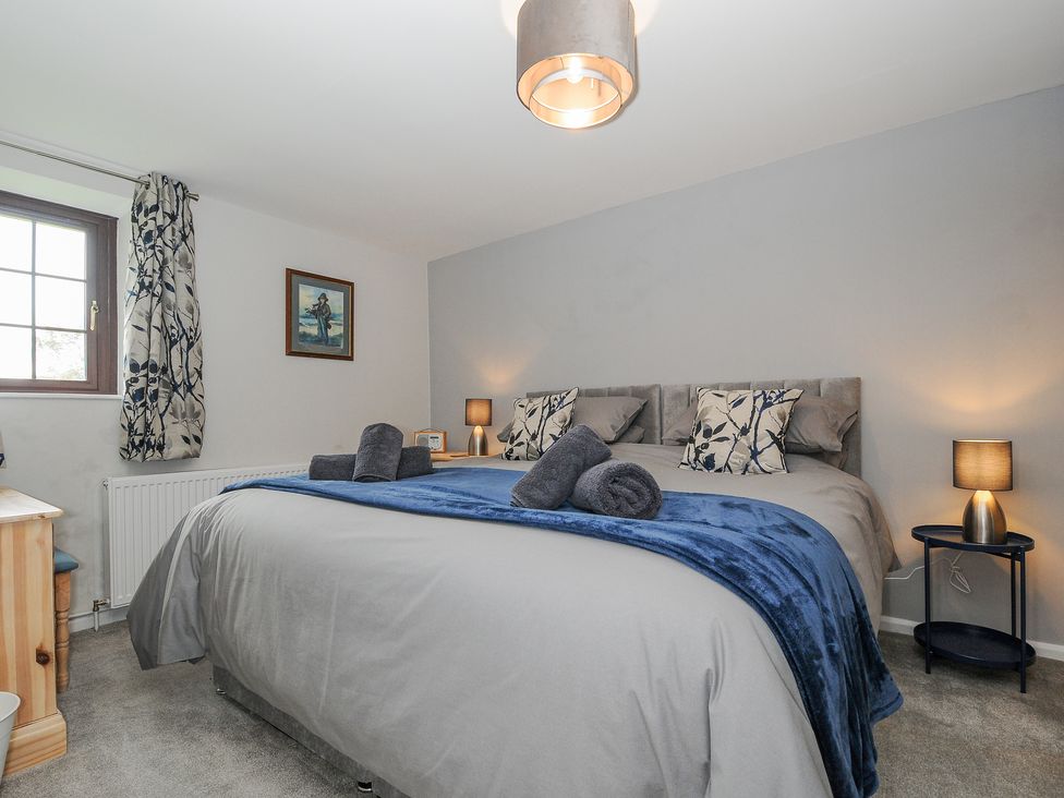 A bedroom with a double bed bedside tables lamps a window with curtains and framed artwork at Manor Barn in Saltash