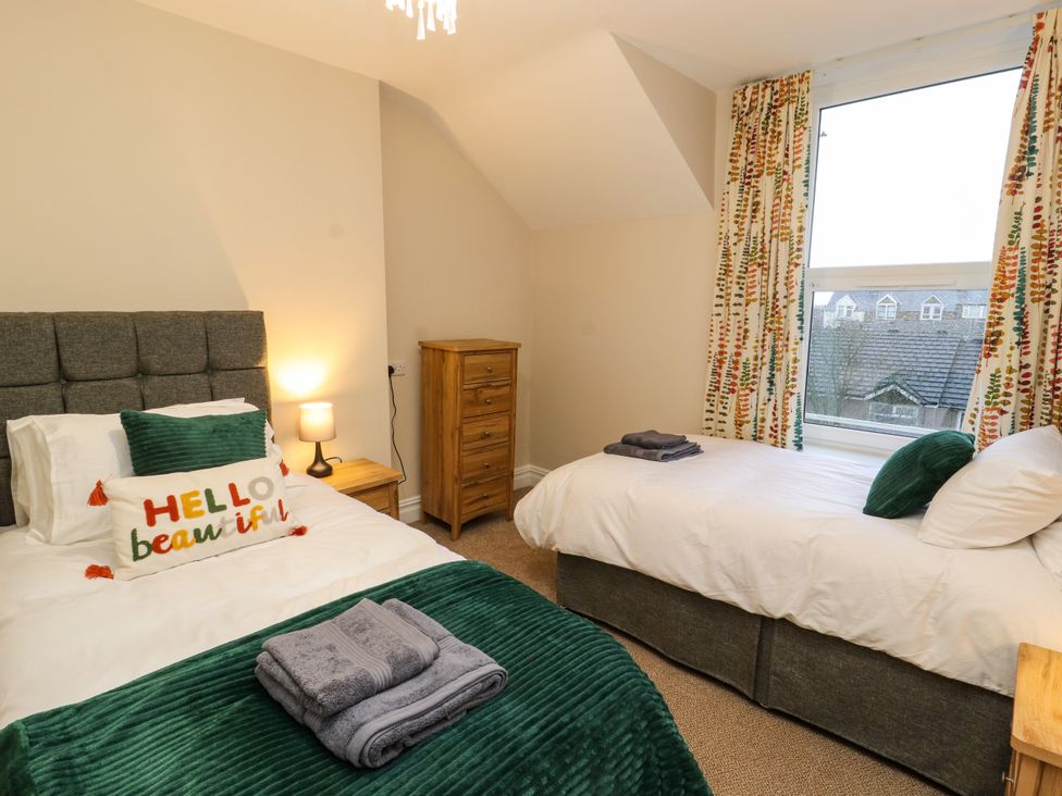 A bedroom with two single beds green throws wooden drawers and window with patterned curtains at Inglemead in Morecambe