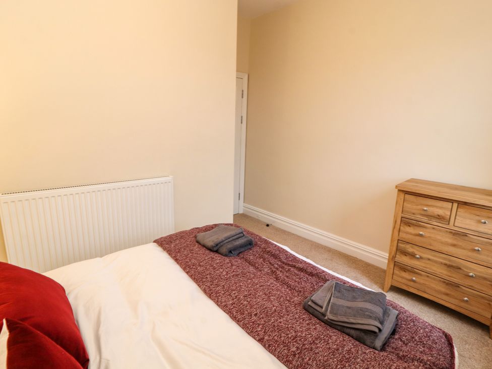 A bedroom with a bed with folded towels on a blanket and a wooden dresser with drawers at Inglemead in Morecambe