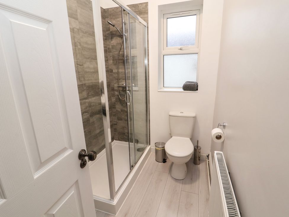 A bathroom with a shower enclosure a toilet a window radiator and a towel at Inglemead in Morecambe