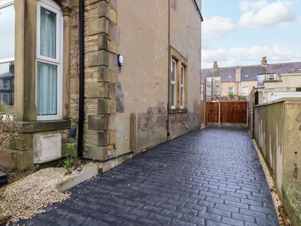 A driveway beside a house with stone walls and windows leading to a wooden gate at Inglemead in Morecambe