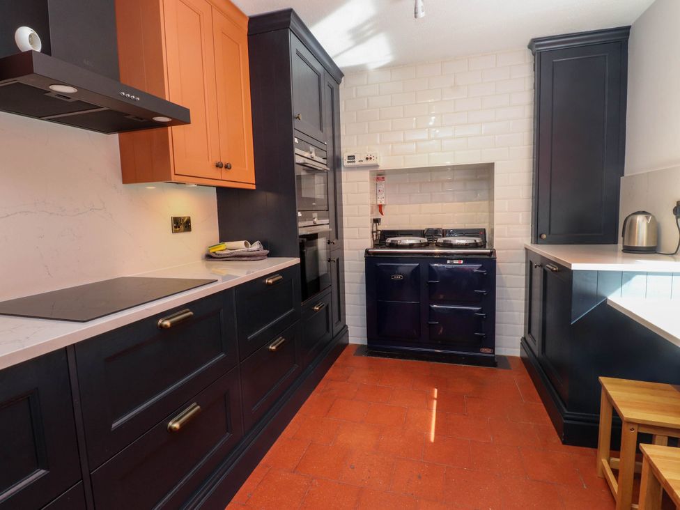 A kitchen with dark blue and orange cabinets a stovetop oven and white tiled walls at Bryn Tirion Morfa Nefyn