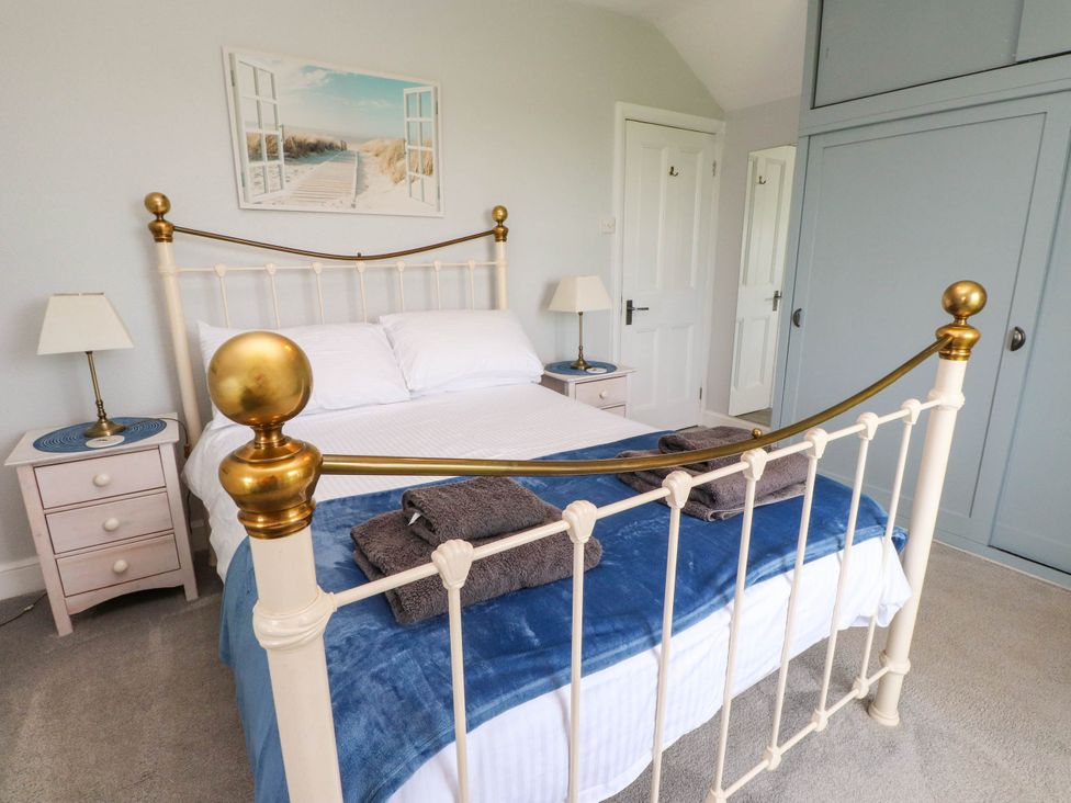 A bedroom with a metal bed frame featuring brass accents a blue blanket and folded towels two bedside tables with lamps a wardrobe and a door at Bryn Tirion in Morfa Nefyn