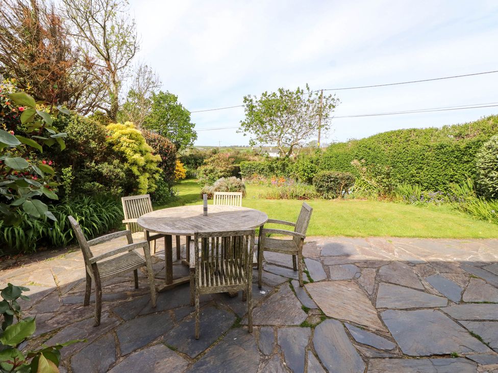A garden with a stone patio and a round wooden table with four wooden chairs at Bryn Tirion in Morfa Nefyn