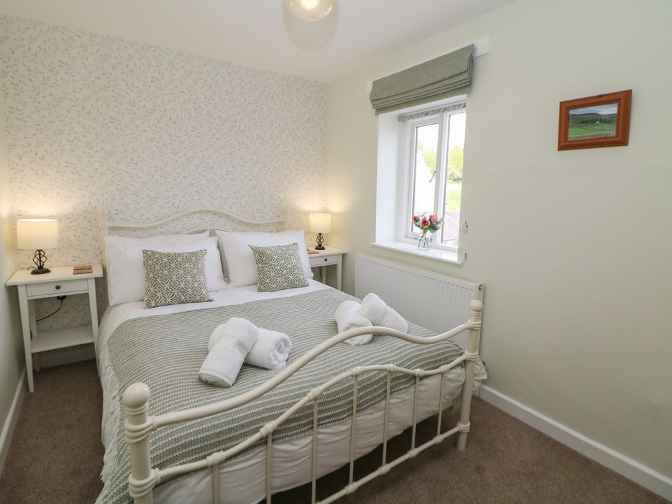 A bedroom with a metal bed frame two bedside tables with lamps a window with a roman blind and a small picture on the wall at The Cottage Bradwell in Bradwell