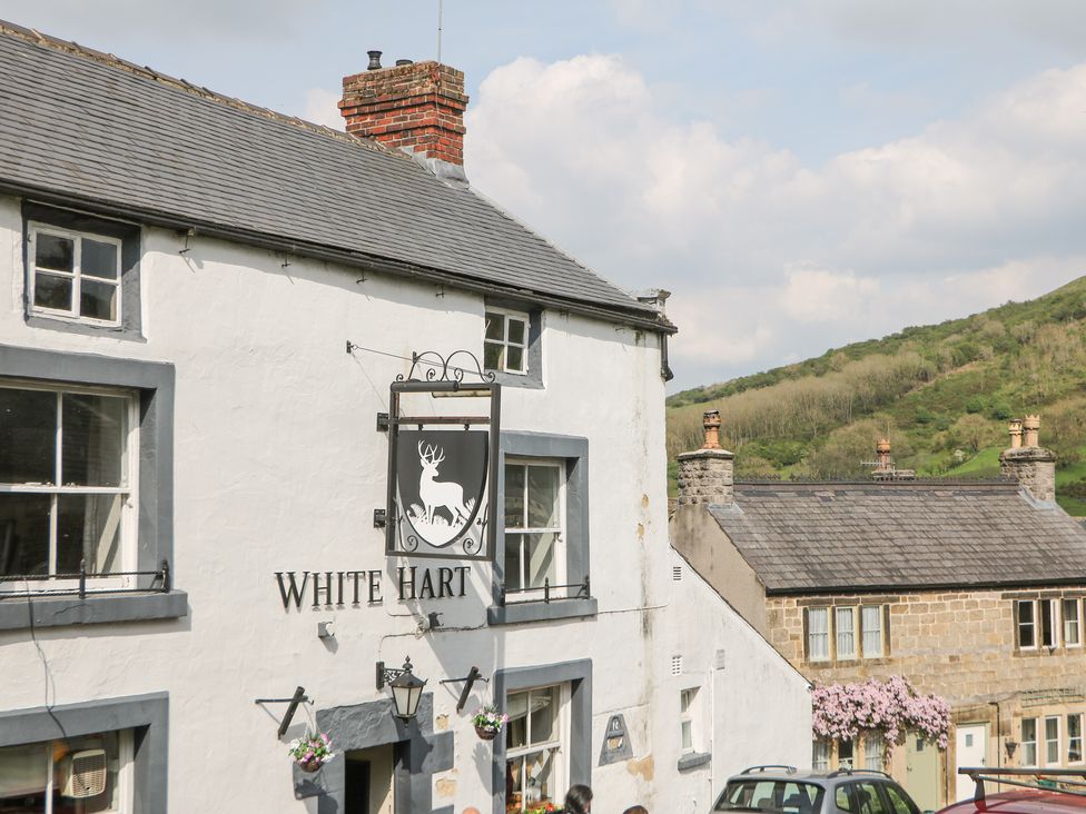 A white building with a sign reading White Hart and a stag image with surrounding buildings and hills in the background at The Cottage Bradwell