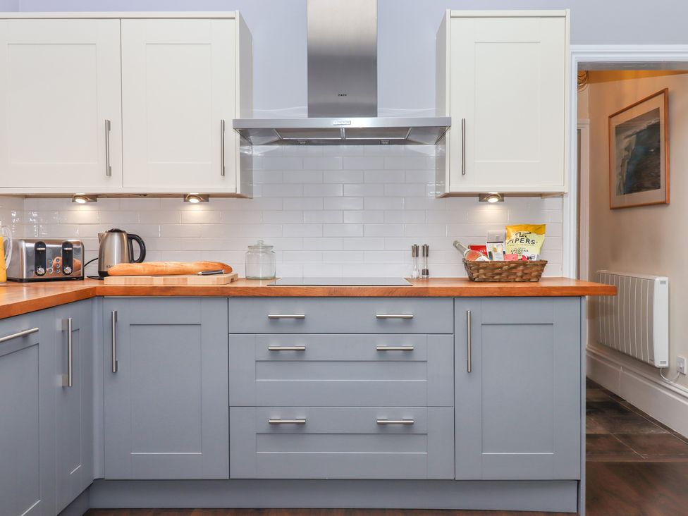 A kitchen with blue lower cabinets and white upper cabinets with wooden countertops at Rockland House in Brixham